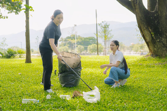 Asian Women Volunteers Collecting Plastic Bottle Garbage into Trash Bag in Green Park for Environmental Protection and Recycling Concept