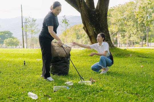 Asian Women Volunteers Collecting Plastic Bottle Garbage into Trash Bag in Green Park for Environmental Protection and Recycling Concept