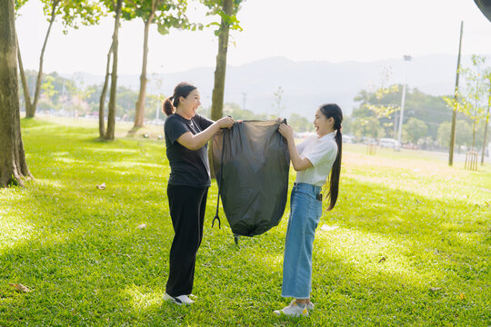 Asian Women Volunteers Collecting Plastic Bottle Garbage into Trash Bag in Green Park for Environmental Protection and Recycling Concept