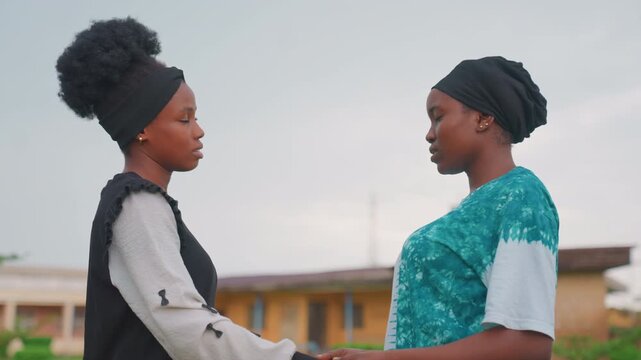 Black mother and child standing holding hands, exchanging serious gaze and quiet promise in open courtyard with overcast sky steady grip, emotional reconciliation and mutual reassurance, intimate