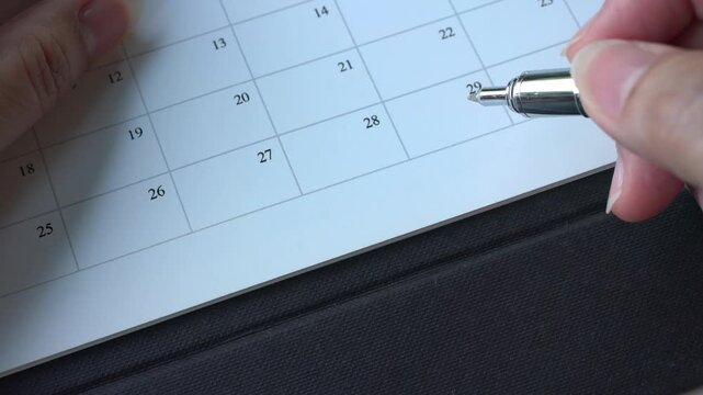 Close up of person going through calendar planner with a pen. Appointments or meeting schedule concept.
