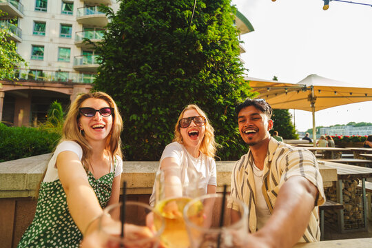 Three smiling young friends celebrating with refreshing drinks on a sunny outdoor terrace