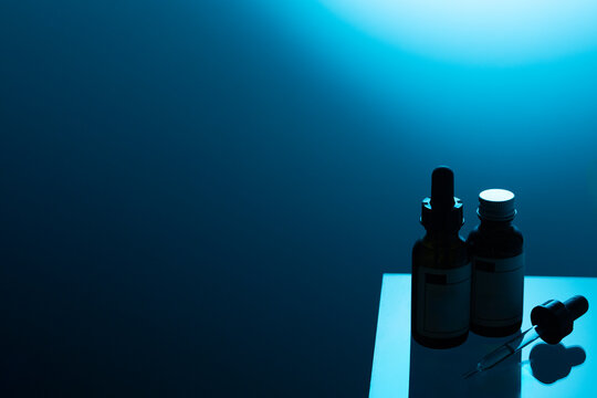 A dark, moody shot of two dropper bottles with blank labels against a deep blue background with an ethereal light, creating a mysterious and modern feel.