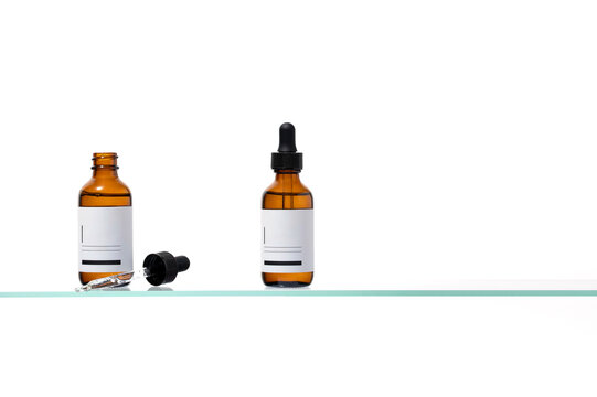 Duo of amber serum bottles on a glass shelf. One is capped, the other open with the pipette exposed. Excellent for comparative cosmetic packaging, branding, and e-commerce visuals.