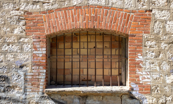 Ventana tapiada de ladrillo rojo y reja de hierro en muro de piedra