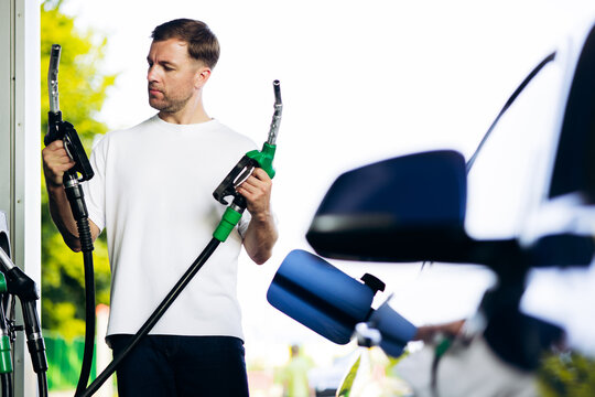 Man at a gas station holding two different fuel nozzles, deciding which type of energy to use for his car
