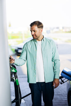 Man fueling car with a green nozzle at a gas station and paying contactless using his smartphone