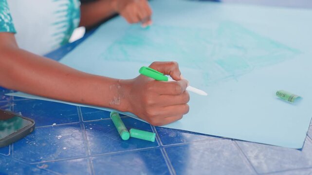 Mother and child drawing on blue paper, closeup hands holding green marker, parent guiding childs stroke, classroom table with stationery, playful warm atmosphere, focus on texture and color, bonding