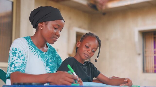 Black mother tutoring child at table, guiding daughter through writing and homework with green marker, focused expressions, warm sunlight on courtyard wall, patient caregiver fostering literacy