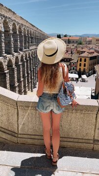 young woman with straw hat looking at the roman aqueduct of segovia spain