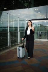 Fototapeta premium Businesswoman on commute transit talking on the smartphone while walking with hand luggage in airpot going to boarding gate. Asian woman happy using mobile phone app for conversation