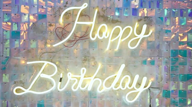 Happy Birthday neon sign on a shimmering sequin wall backdrop for party event decoration.