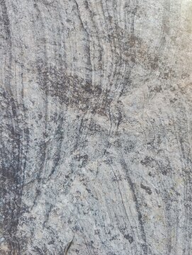 Natural rock surface with layered mineral patterns, rough weathered texture, and earthy gray and brown tones. Organic stone background for architecture, construction and interior design