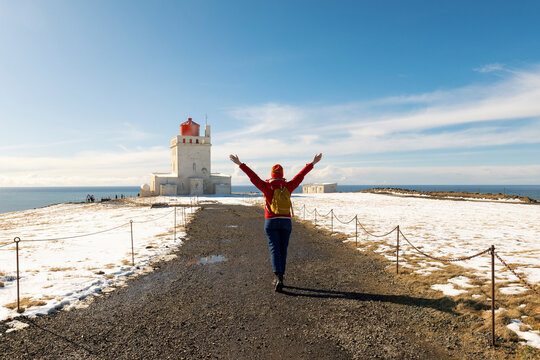 Rear view of young female tourist visiting Dyrholaey Lighthouse located on the top of the cliff in Iceland near Vik I Myrdal village