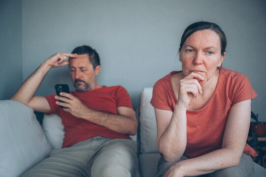 Distant couple sitting on sofa during relationship strain while man focuses on phone
