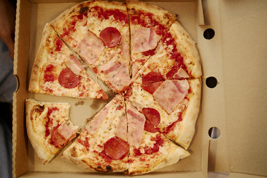 Sliced pepperoni and ham pizza sitting in open cardboard delivery box, representing fast food convenience. Image suitable for food delivery service marketing and restaurant promotions