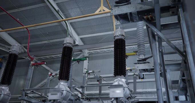 High voltage insulators and conductors hanging from ceiling inside industrial electrical substation interior showing busbars.