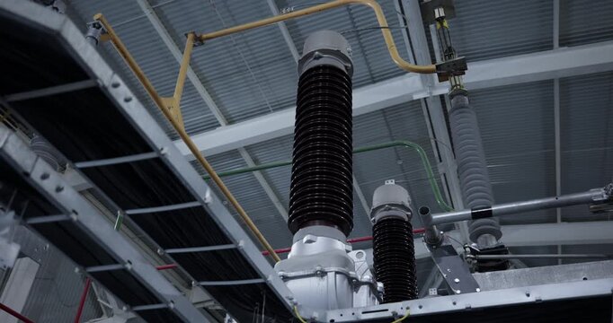High voltage insulators and electrical busbars inside industrial substation ceiling.