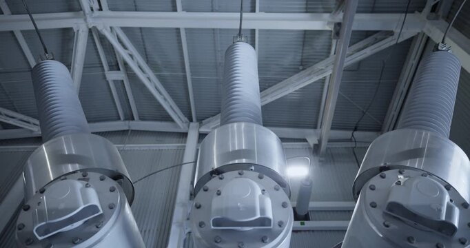 High voltage insulators and metal flange joints inside industrial warehouse ceiling.