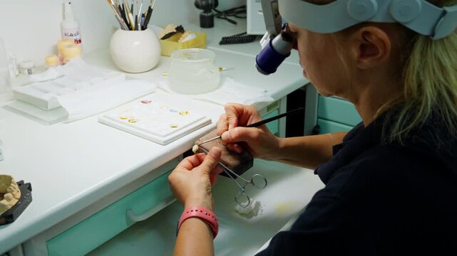 Dental technician carefully painting a dental prosthesis at a laboratory workbench