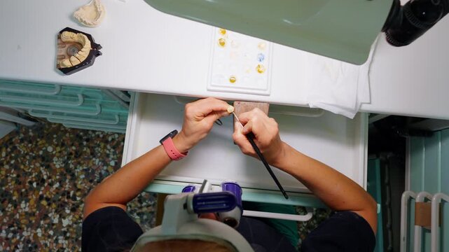 Overhead view of a woman crafting a dental prosthesis at a workbench in a clinic