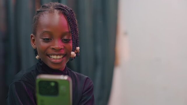 Black girl practicing performance on phone, smiling while rehearsing monologue, braided beads, closeup portrait against curtain backdrop, focused expression, youthful ambition, studio lighting,