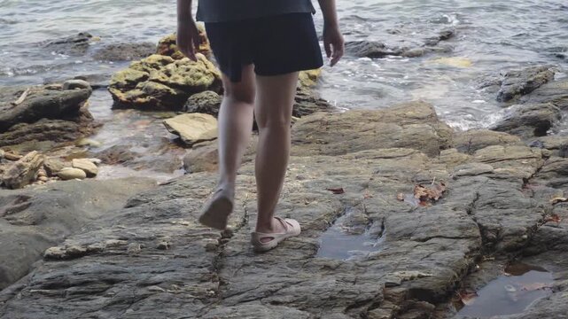 A close up lower body shot of a traveler's footsteps walking across the rocky shoreline towards the ocean waters of Khao Laem Ya Mu Ko Samet National Park in Thailand