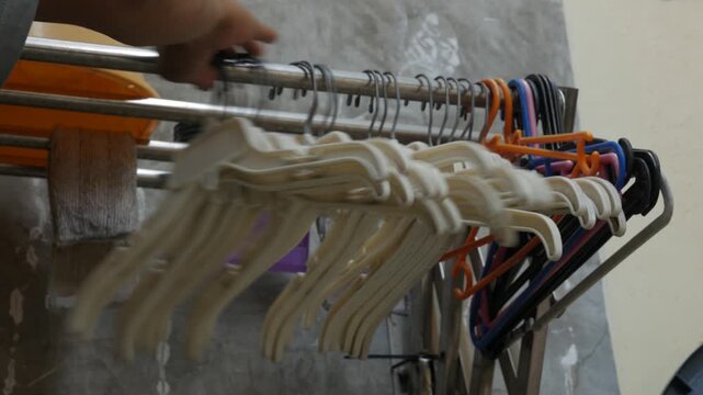 Hand Organizing Plastic Clothes Hangers on a Laundry Rack Close Up