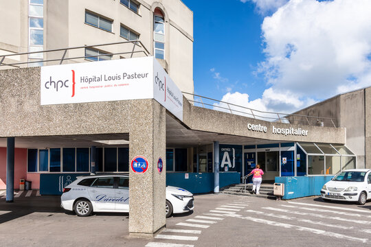 Cherbourg, France - July 20, 2026: A woman head for the main entrance of the Louis Pasteur Hospital, part of the Cotentin Public Hospital Center, as a light medical vehicle is stationing.