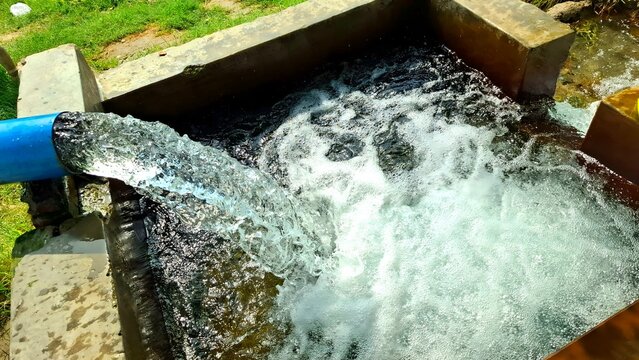 Fresh water flowing from a blue pipe into a concrete reservoir tank for irrigation