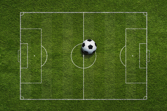Top view of soccer game field with soccer ball on grass and white lines.