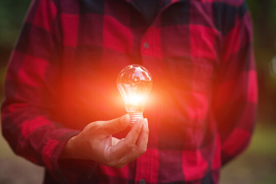 Man in Plaid Shirt Holding Glowing Light Bulb for Energy and Innovation Concept