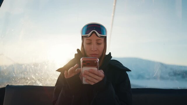 Good internet and mobile net coverage area, use smartphone at top of mounts. Woman skier or snowboarder riding cable car in modern luxury ski resort, watching pictures on screen, phone addiction