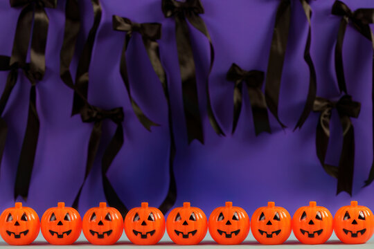 Halloween decor with row of small jack o lantern pumpkins and black ribbons on purple background