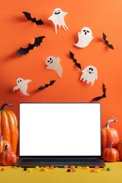 Laptop mockup with blank white screen surrounded by Halloween pumpkins, ghosts, bats, and candy