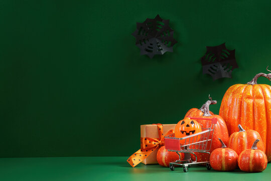 Halloween shopping concept with pumpkins, gift box, and mini shopping cart on green background