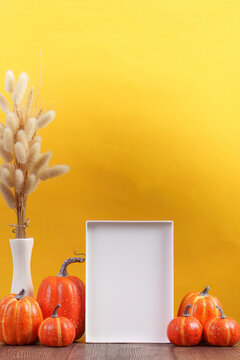 Autumn decor frame mockup with decorative orange pumpkins and dried grass on yellow background