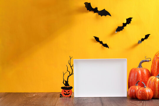 Halloween concept with blank frame mockup, orange pumpkins and bats on yellow background