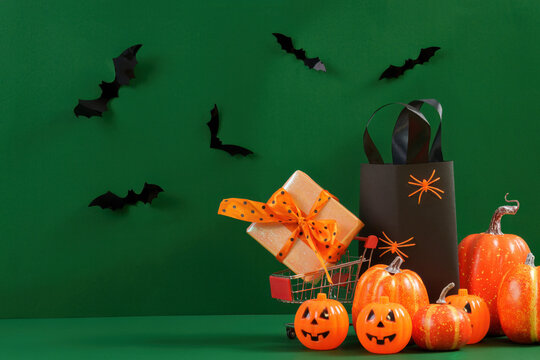 Halloween shopping and sale concept with gift box bag and pumpkins on green background