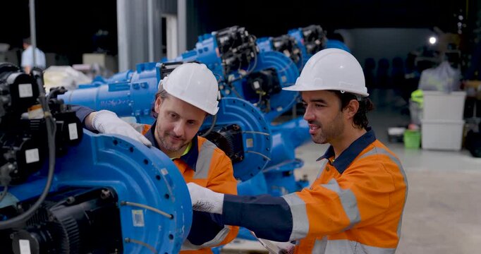 Two adult male technicians inspect industrial robotic arm joint in factory workshop, touching mechanical components and discussing equipment condition during preventive automation maintenance service.