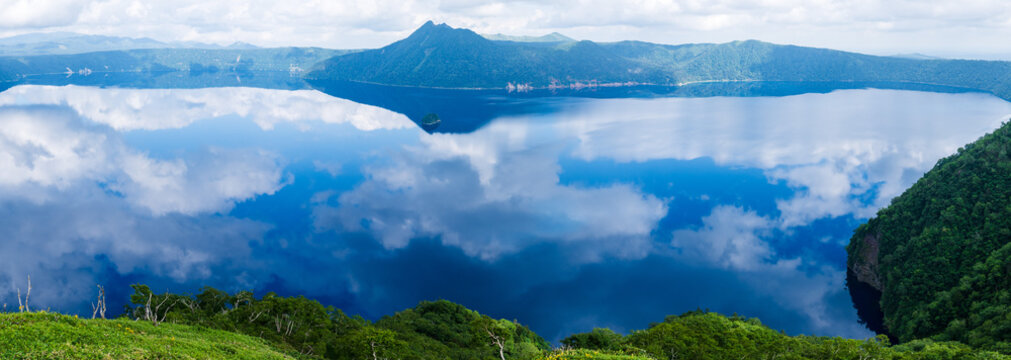 Wide panorama of clouds reflected across Lake Mashu caldera in Hokkaido