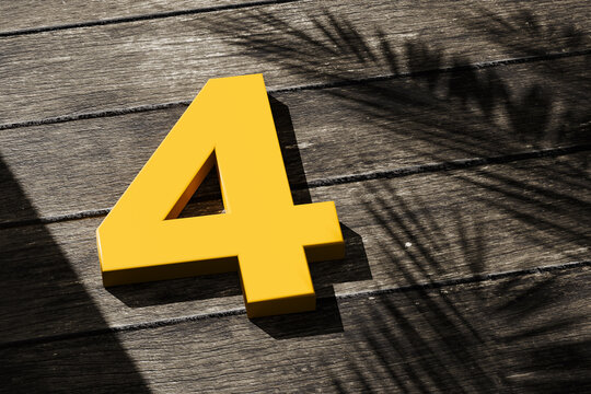 Yellow number four on wooden surface with palm shadow