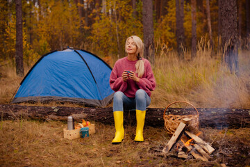 woman relaxing near campsite tent with warm cup by teepee campfire in fall forest © cenchild