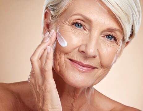 Retrato en primer plano de una mujer senior con una piel facial envejecida pero saludable d&aacute;ndose crema rejuvenecedora sobre la piel