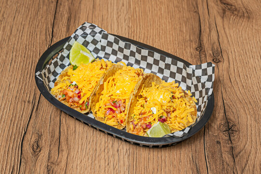 Three cheese-topped chicken tinga tacos with lime wedges served in a checkered-lined food basket.