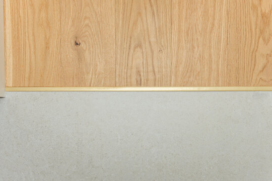 Straight-on view of oak flooring transitioning to grey tile via a horizontal brass threshold strip.