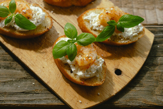 Bruschetta with cream cheese, shrimp and fresh basil on wooden board. Tasty snacks.