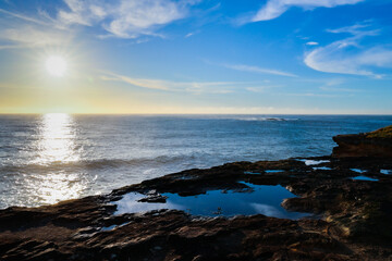 Obraz premium Scenic coastal view across natural rock pools and the Pacific Ocean near Giles Baths at Coogee in Sydney, Australia, illuminated by morning sunlight.