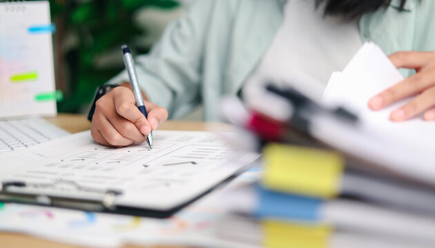 Business professional reviewing documents and writing notes at an office desk, with folders and laptop nearby, representing business planning, research, productivity, organization, and workflow.