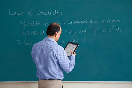 Teacher with digital tablet writing on blackboard